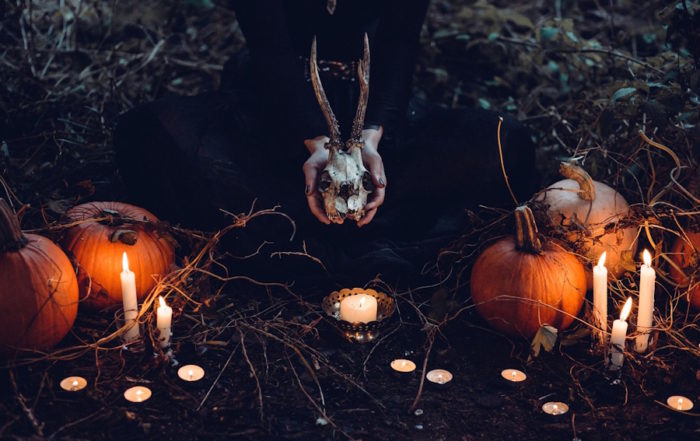 Halloween in Köln: Eine Person, die einen Hirschschädel hält, umgeben von Kürbissen und Kerzen in einer dunklen, natürlichen Umgebung.