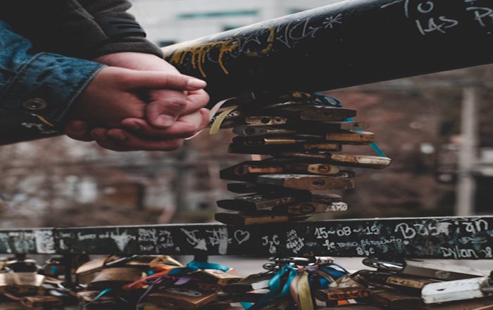 Unschuldige Liebe: Zwei Menschen, die sich an einer Brücke voller Liebesschlösser die Hände halten.