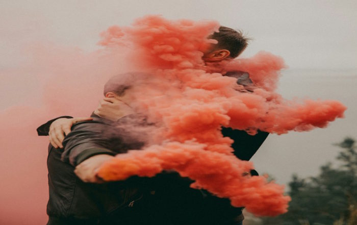 Amor Inocente: Una pareja abrazándose rodeada de vibrante humo rojo.