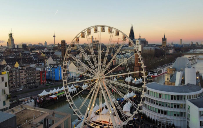 Tour-Reise in Köln: Ein lebhaftes Riesenrad steht prominent vor der Skyline der Stadt und zeigt urbanen Charme und Aufregung.