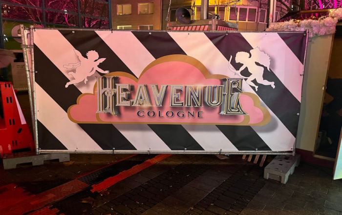 Heavenue Köln Branding: Offizielles Weihnachtsmarkt-Schild mit Engel-Silhouetten und Streifen-Design